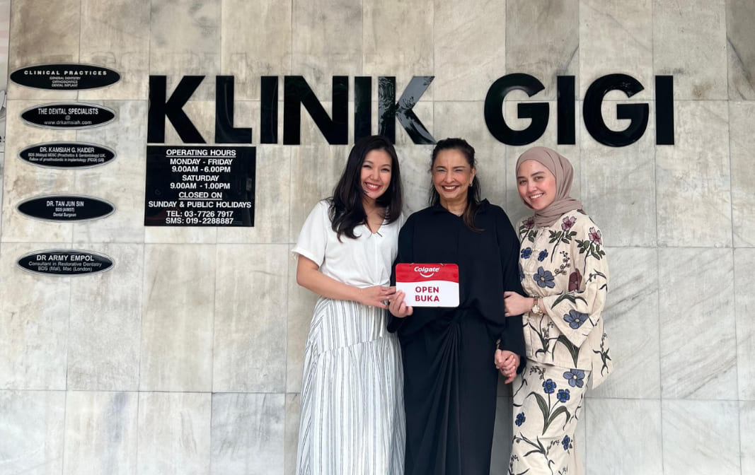 Team photograph of Dr Kamsiah and colleagues beneath historical Klinik Gigi signage